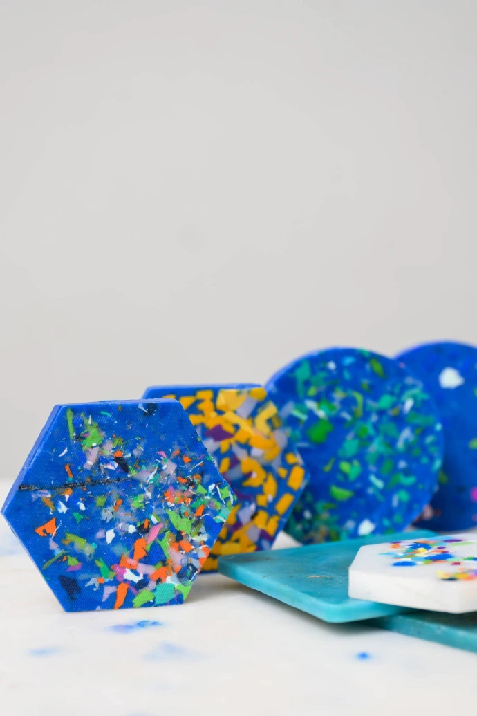 A lineup of recycled plastic coasters in hexagonal, circular, and square shapes showing geometric variety.
